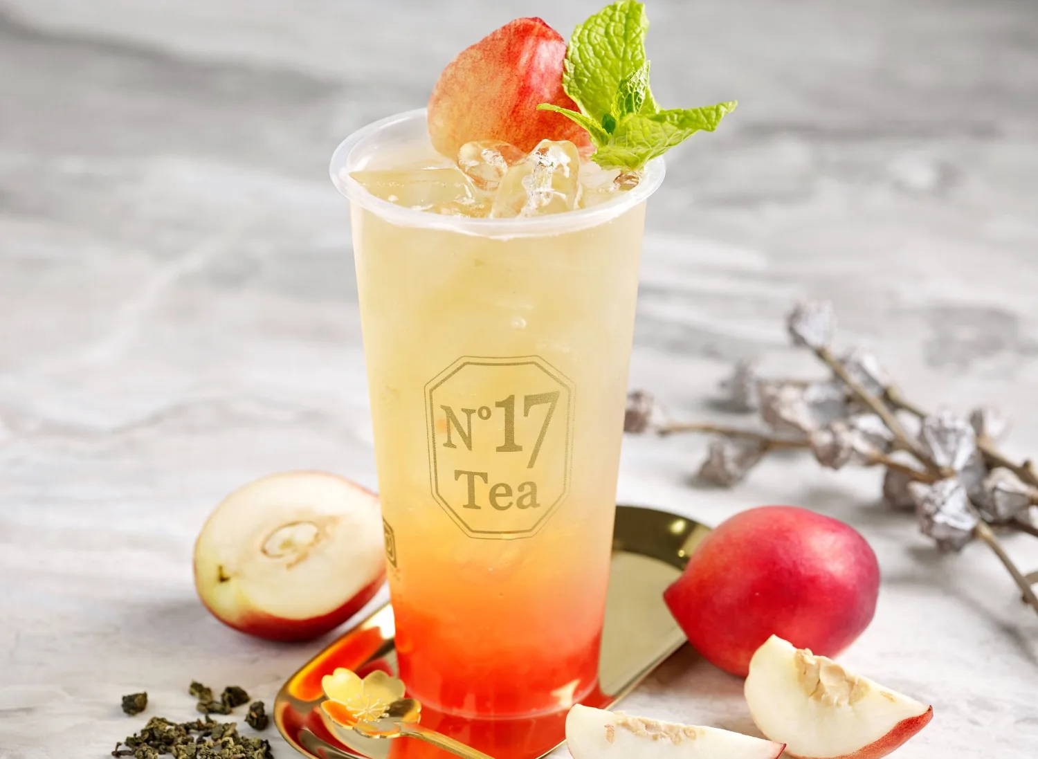 White Peach Oolong in a gold-logo No.17 Tea cup, garnished with white peach and mint, with fresh peaches and oolong leaves on marble